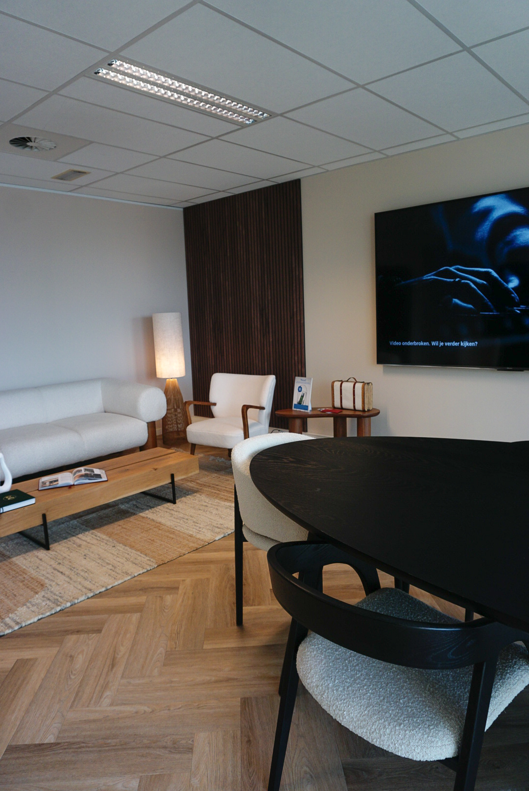 Zithoek in de wachtruimte van MED-CLINIC Antwerpen met een wandscherm, houten lattenwand, crèmekleurige zetel en een zwarte overlegtafel.