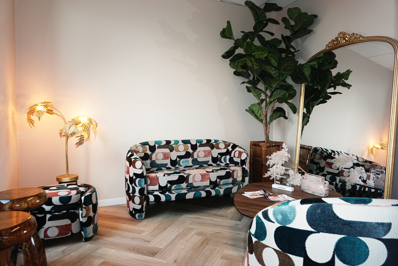 Wachtruimte van MED-CLINIC Antwerpen met een gedessineerde zitbank, staande gouden spiegel en een grote vioolbladplant.