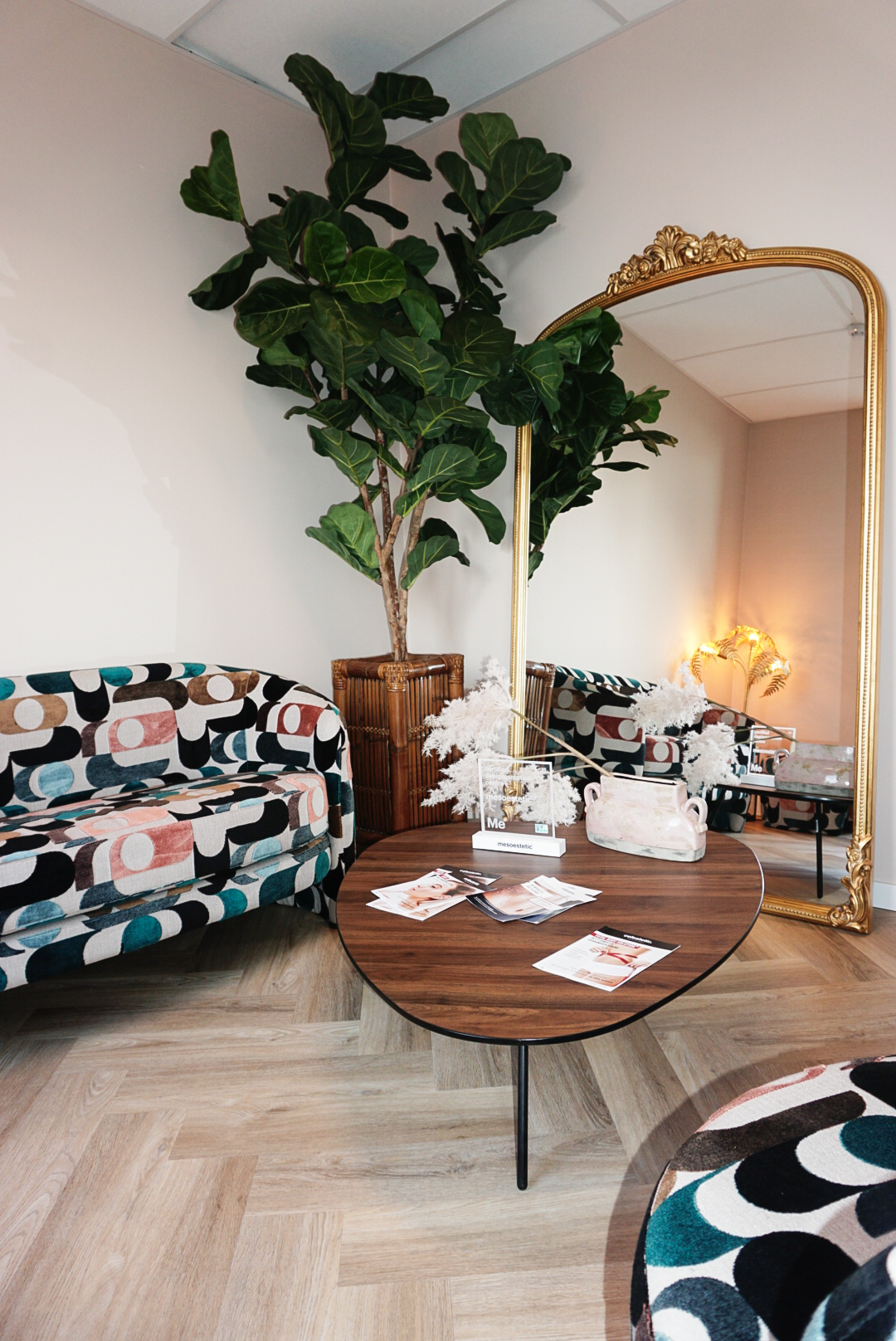 Wachtruimte van MED-CLINIC Antwerpen met ronde houten salontafel, informatiefolders, gedessineerde zitbank en een gouden spiegel.