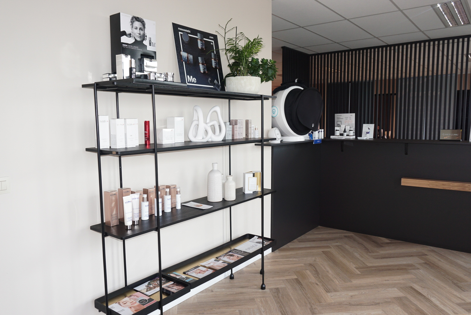 Inkom van MED-CLINIC Antwerpen met zwart productrek, verzorgingsproducten en de onthaalbalie met huidanalysetoestel op de achtergrond.